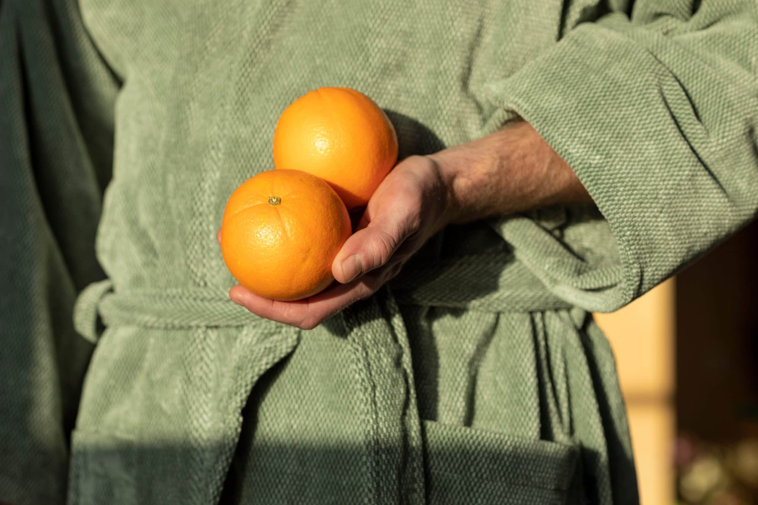 Two,Oranges,In,A,Mans,Hand,In,A,Green,Blanket